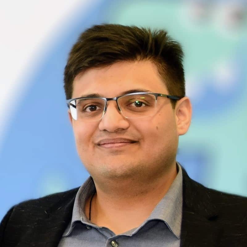  A man in glasses smiling and looking down the camera.