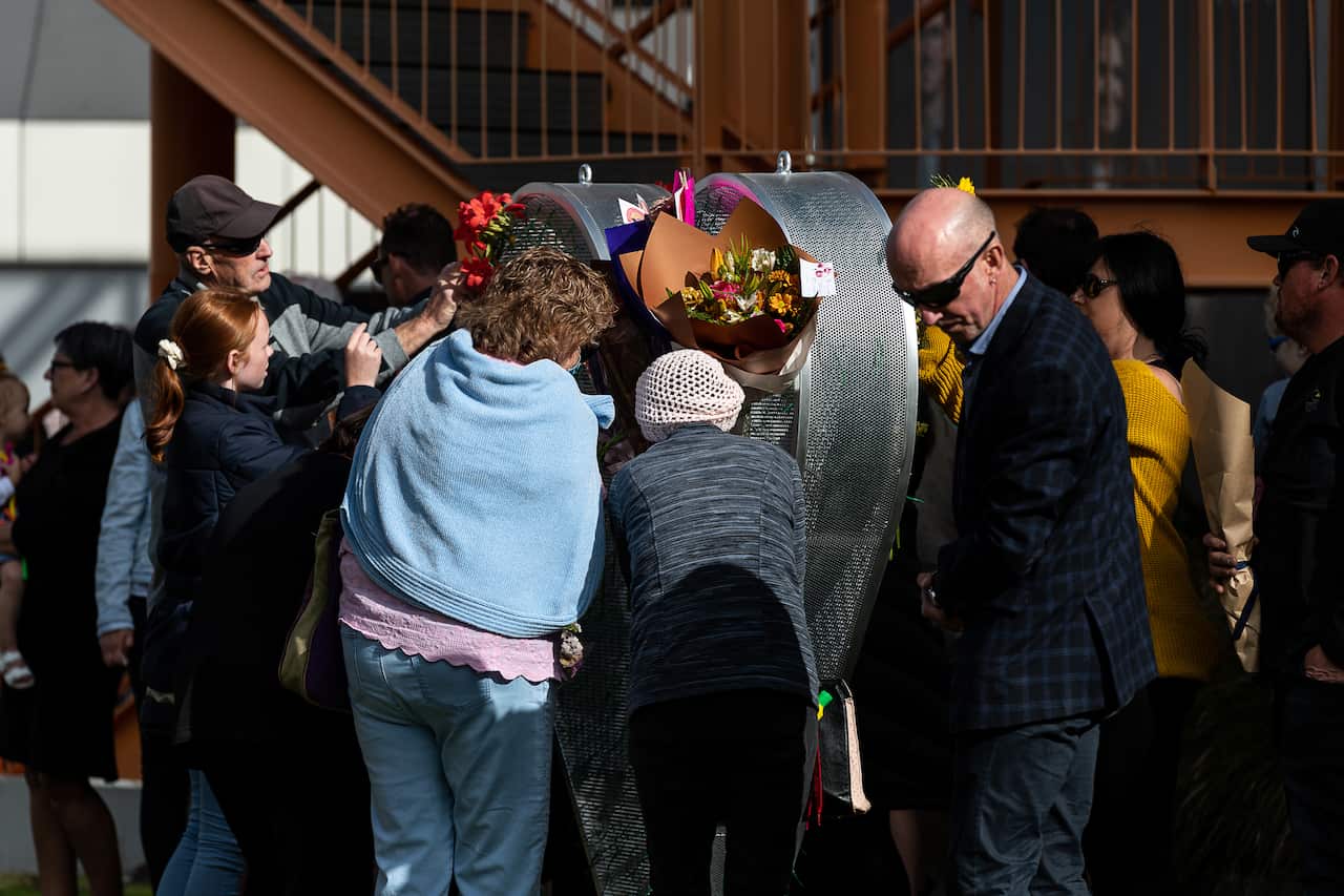 People placing flowers on a heart-shaped structure.