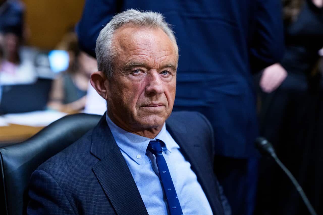 RFK Jr looks grim in a blue suit with speckled blue tie while sitting in a commitee