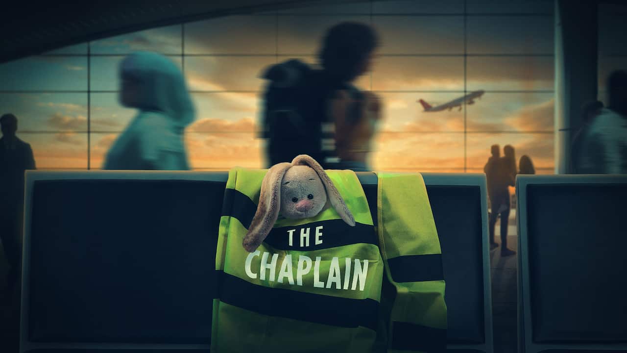 A high-visibility vest with the word Chaplain on it hangs on a railing. A plane can be seen in the background. 