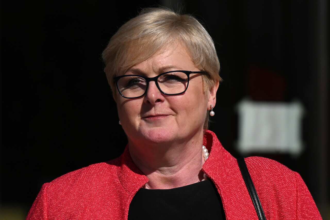 A woman wearing glasses, a black top, and a red blazer.