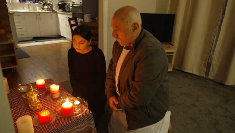 A girl and a man sit solemnly in front of candles.