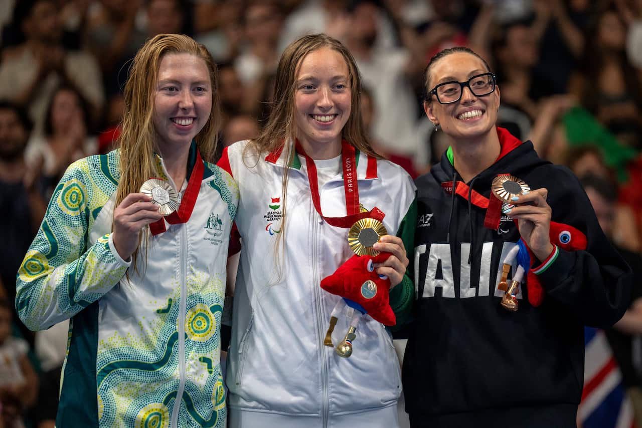 Three medallists hold up their silver, gold and bronze medals. A crowd is seated behind them.