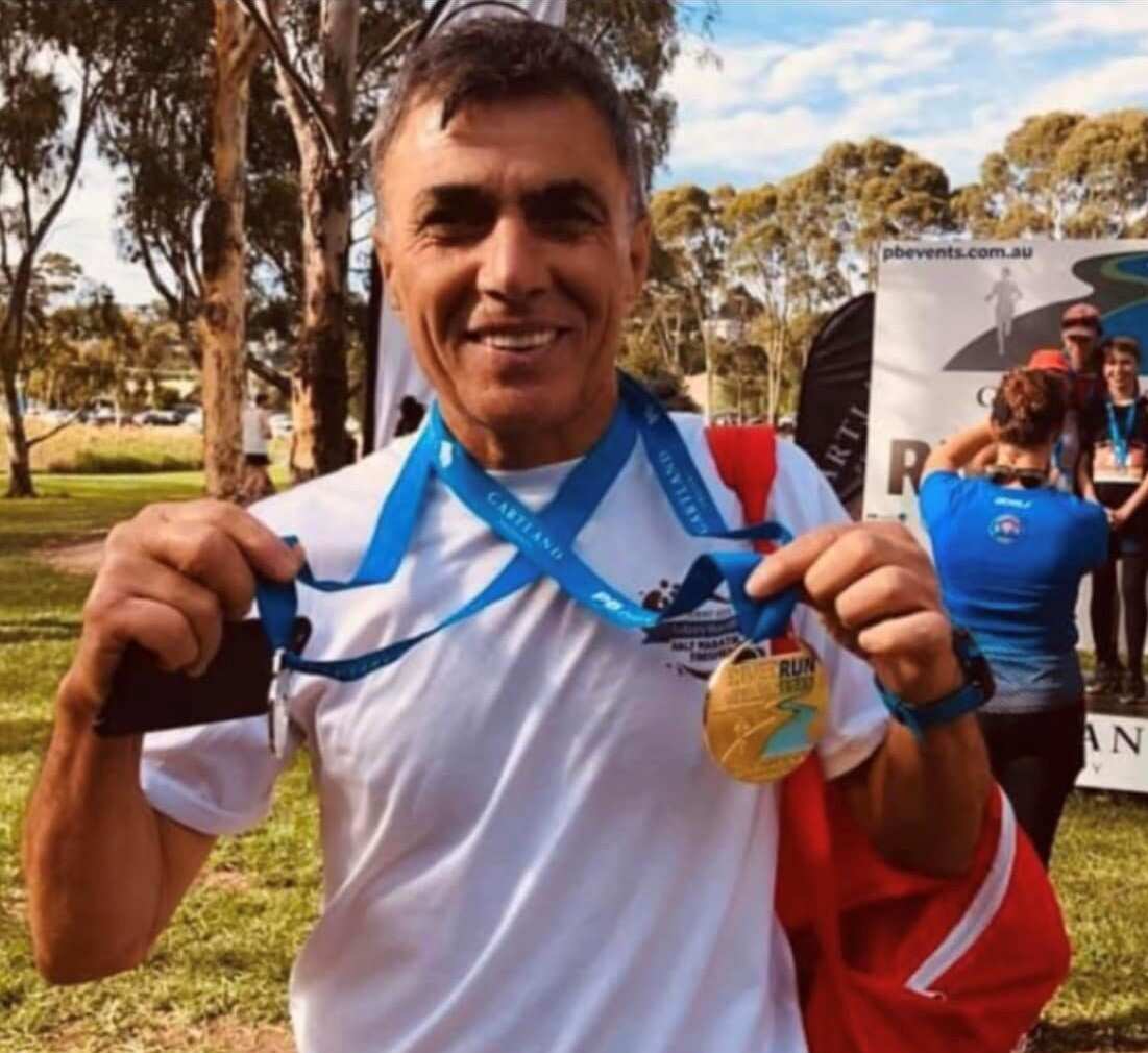 A man holds up two medals that are hung around his neck