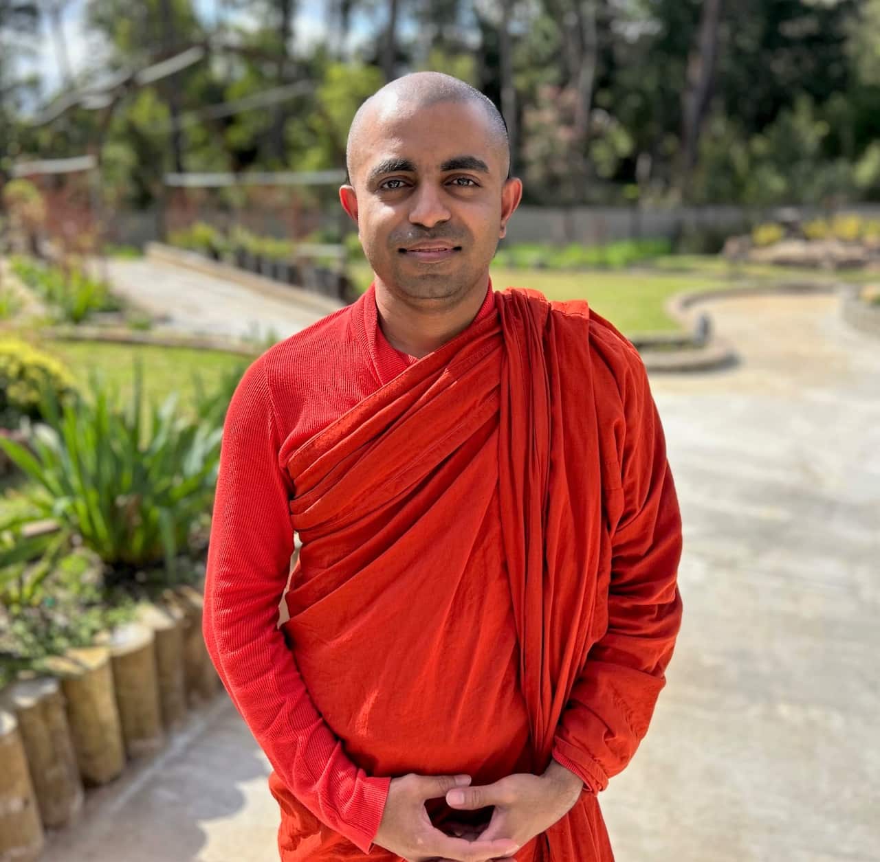 A man in an orange robe stands on a pathway facing camera. 