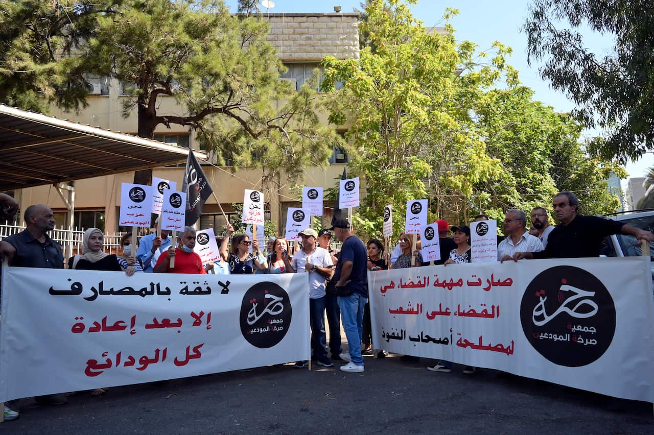 A group of people standing outside. Some are holding two large banners featuring writing in Arabic, while others are holding placards with writing in Arabic. 