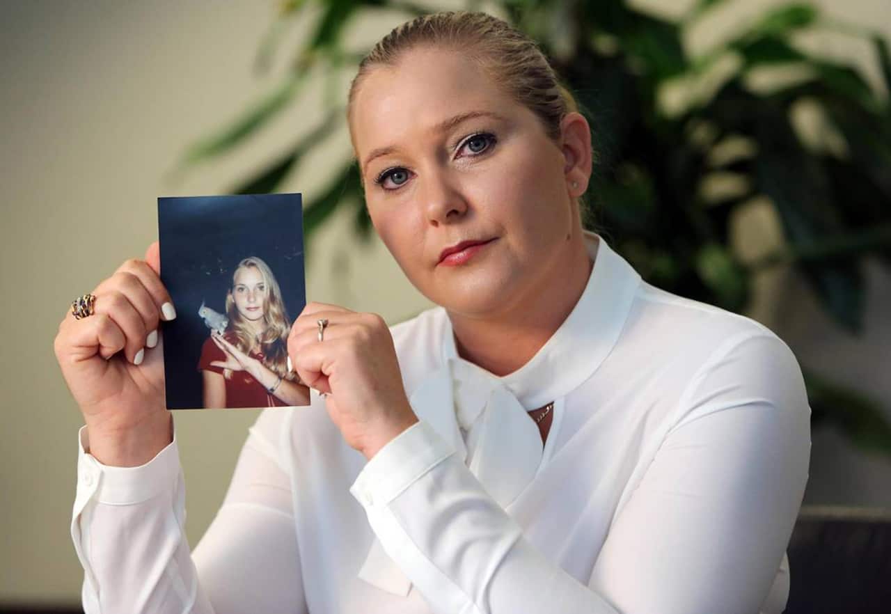 A woman wearing a white top, holding up a photograph of herself much younger.
