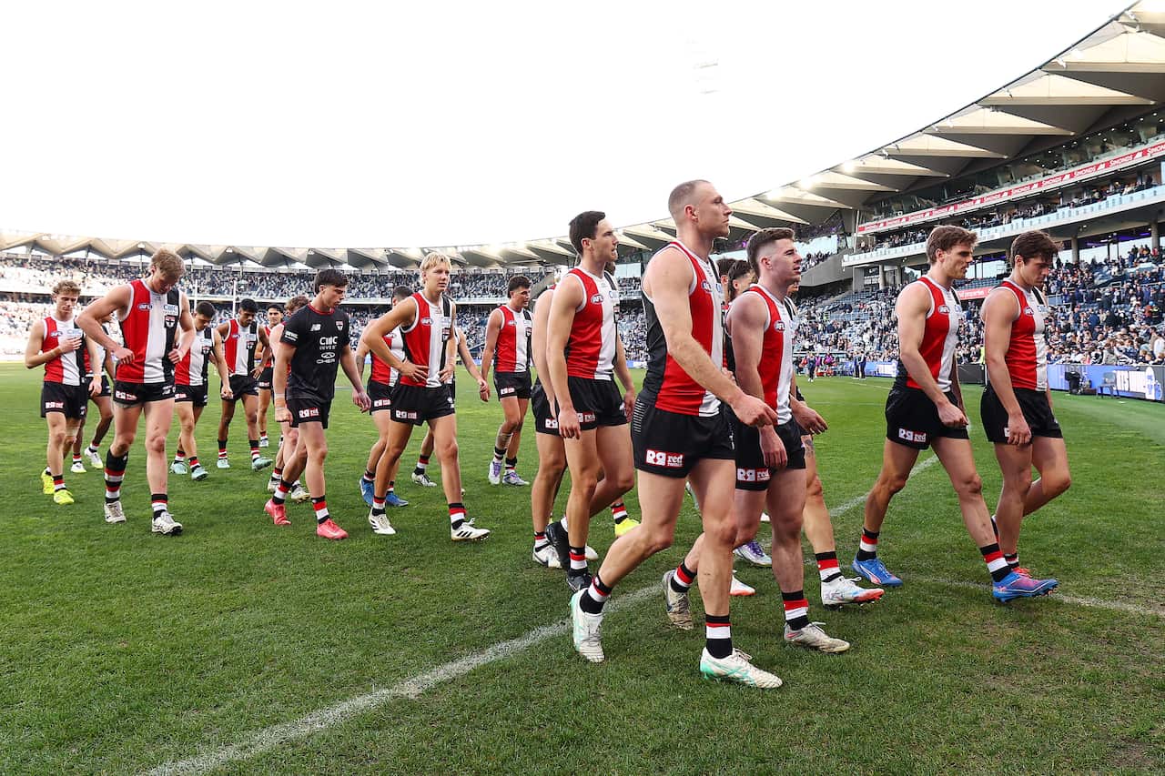 A group of men dressed in AFL uniforms walk off the field in a crowded stadium. 