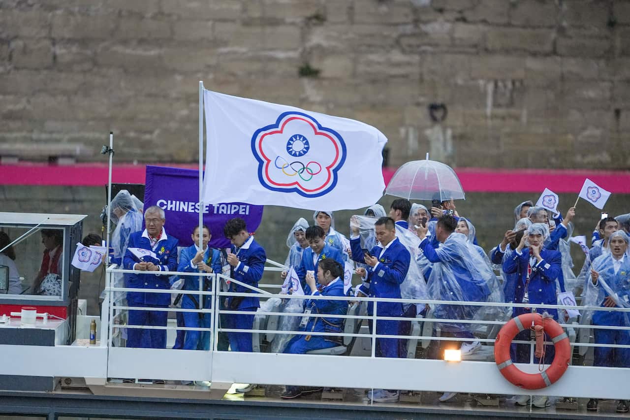 Athletes from the Chinese Taipei Olympic Team sail in a boat along the river Seine holding up their team flag.