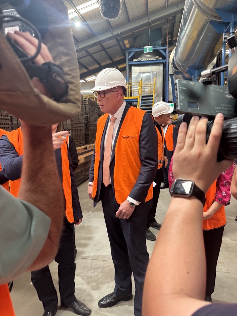 Peter Dutton wearing a hard hat and a hi-vis vest on a visit to a brick factory.