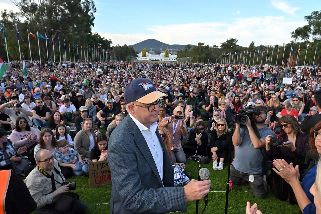 A man in a cap stands in front of a large group of people