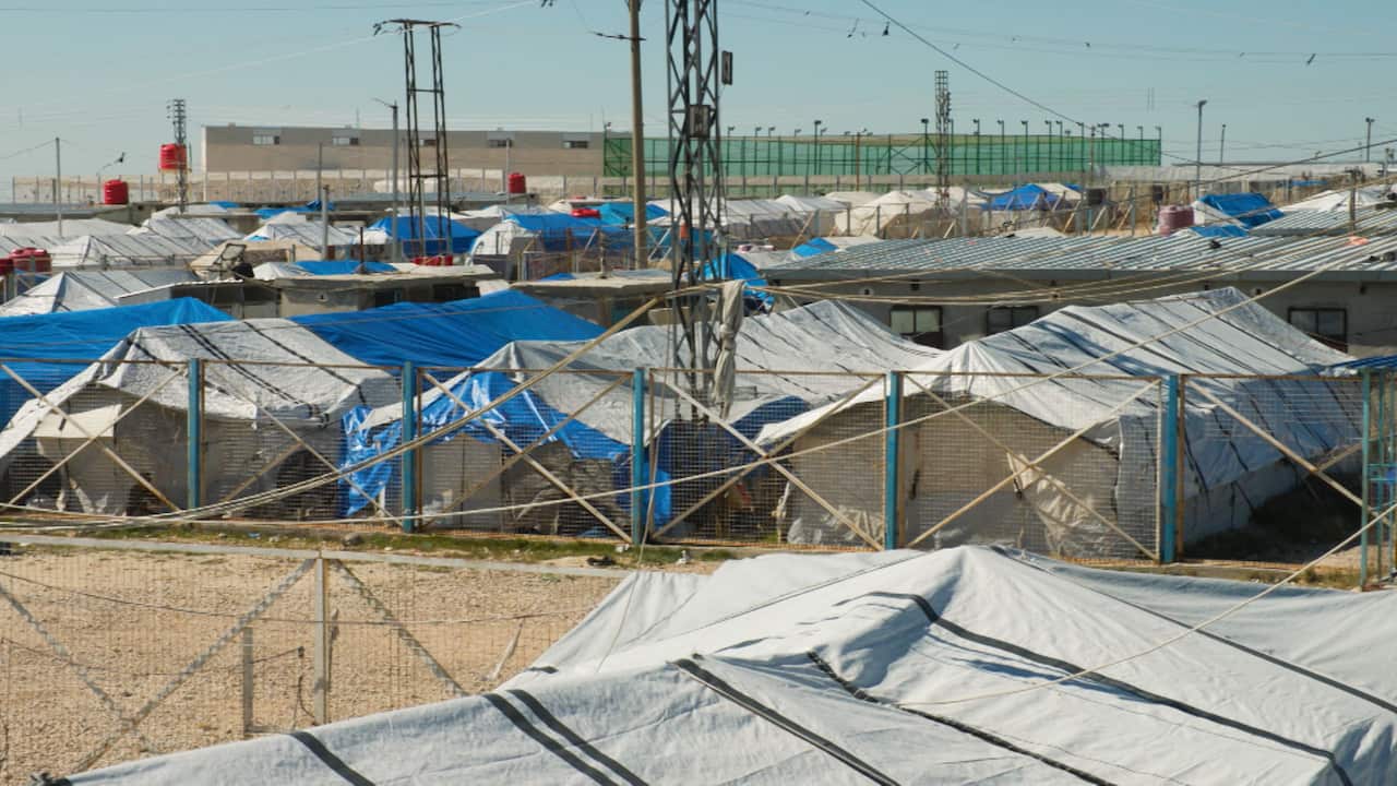 Makeshift tents in a refugee camp surrounded by a fence 