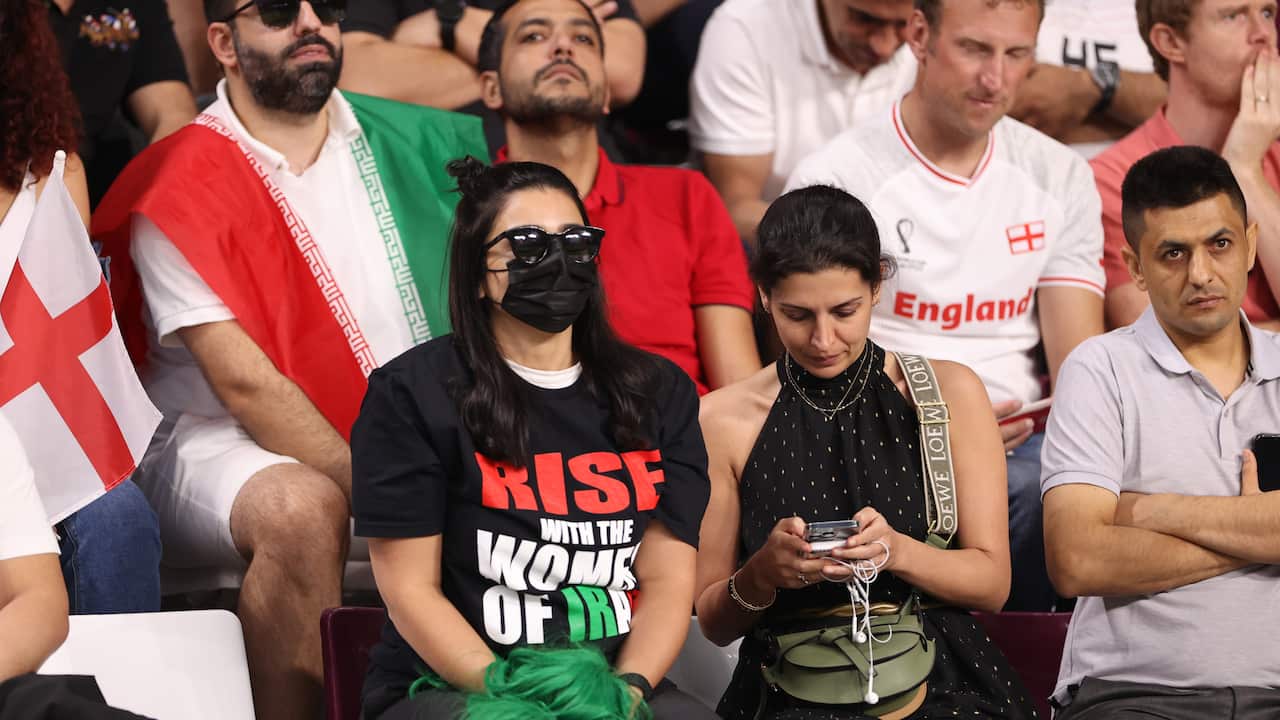 A woman sits in a crowd wearing a tshirt which reads 'Rise with the women of Iran'