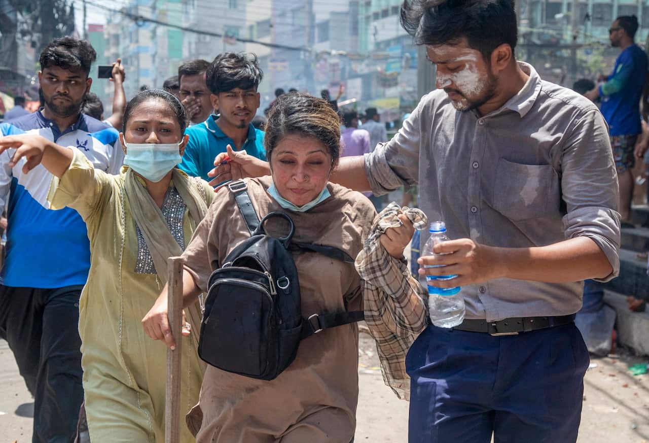 Three students run away from police officers using tear gas. One of the students is holding an arm around a student while also holding a bottle of water.