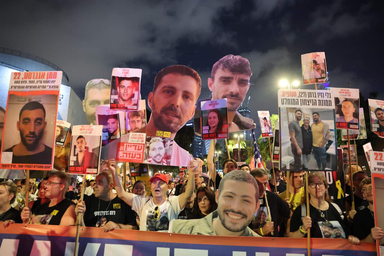 A group of protesters hold up placards with images of people's faces and Hebrew writing.