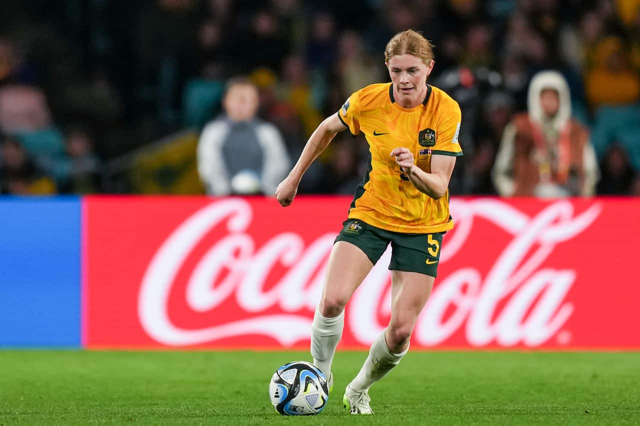 A woman in a yellow football shirt kicking a ball.