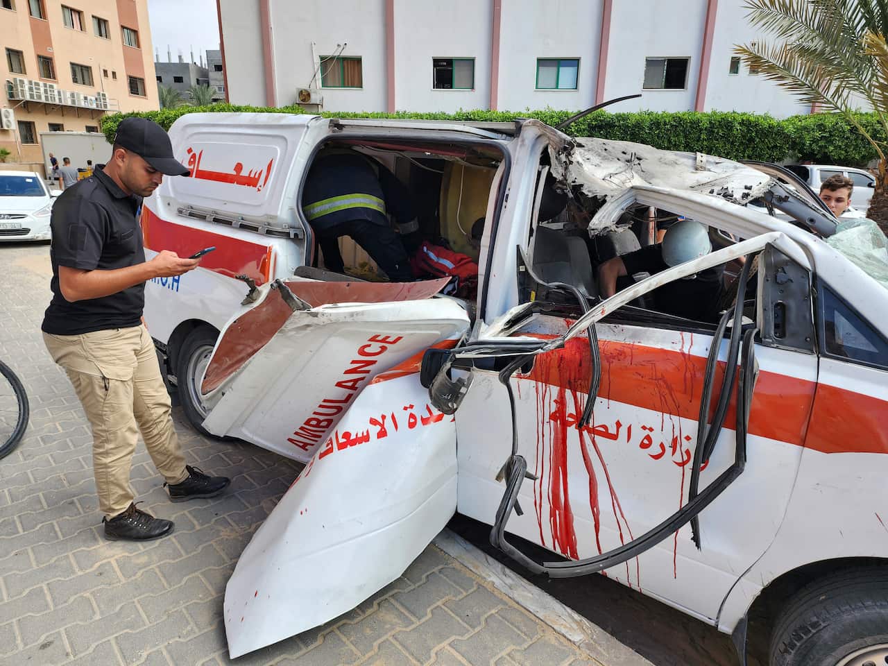 Palestinian medics inspect a damaged ambulance. The ambulance is crushed and there are bloodstains on the door.