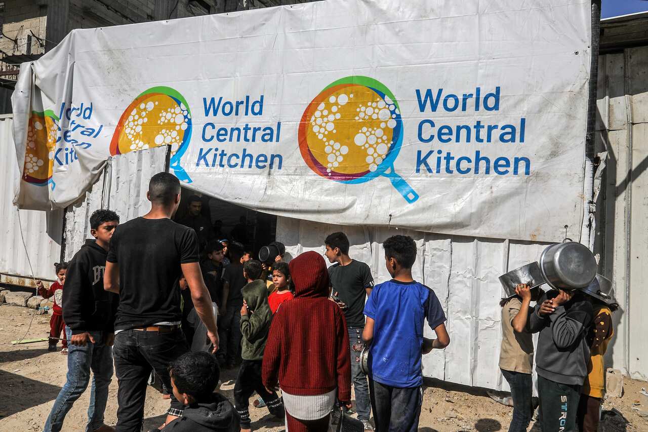 A small group of young people facing a banner that reads World Central Kitchen. Some are carrying pots