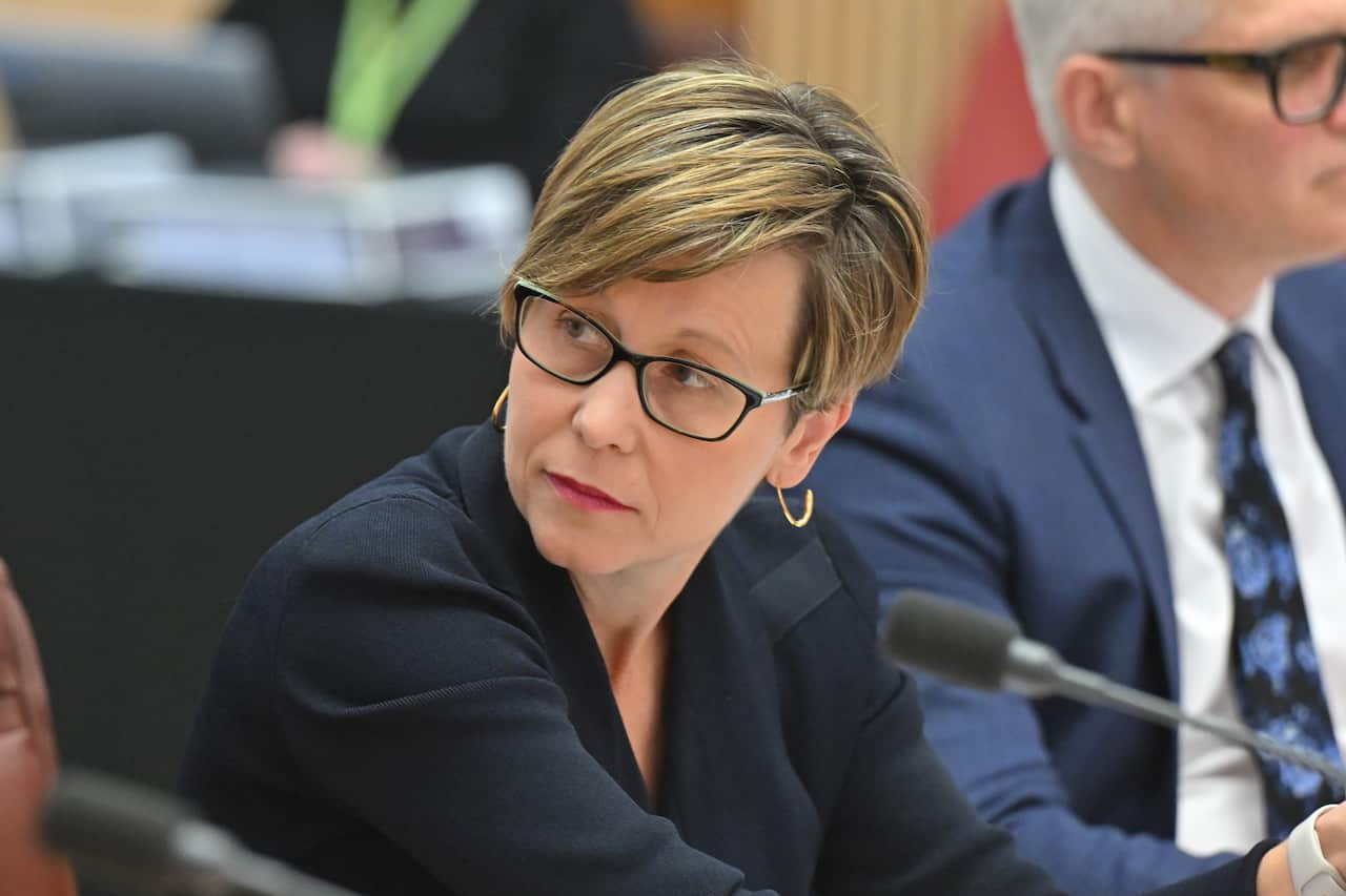 A woman with cropped hair and a blue blazer sits in front of a microphone 