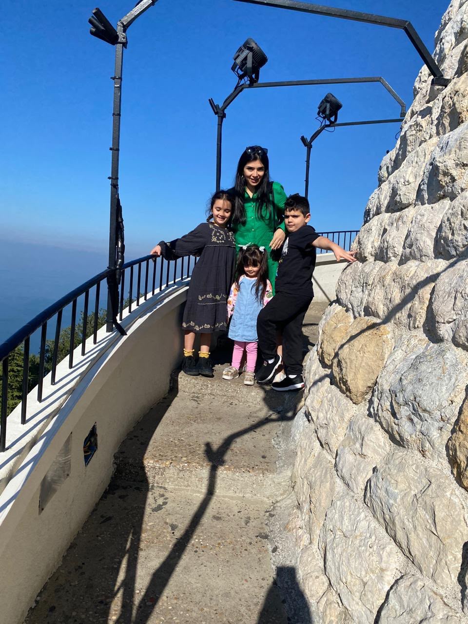 A woman in a green dress stands on the stairs of a circular structure with her two daughters and a son.