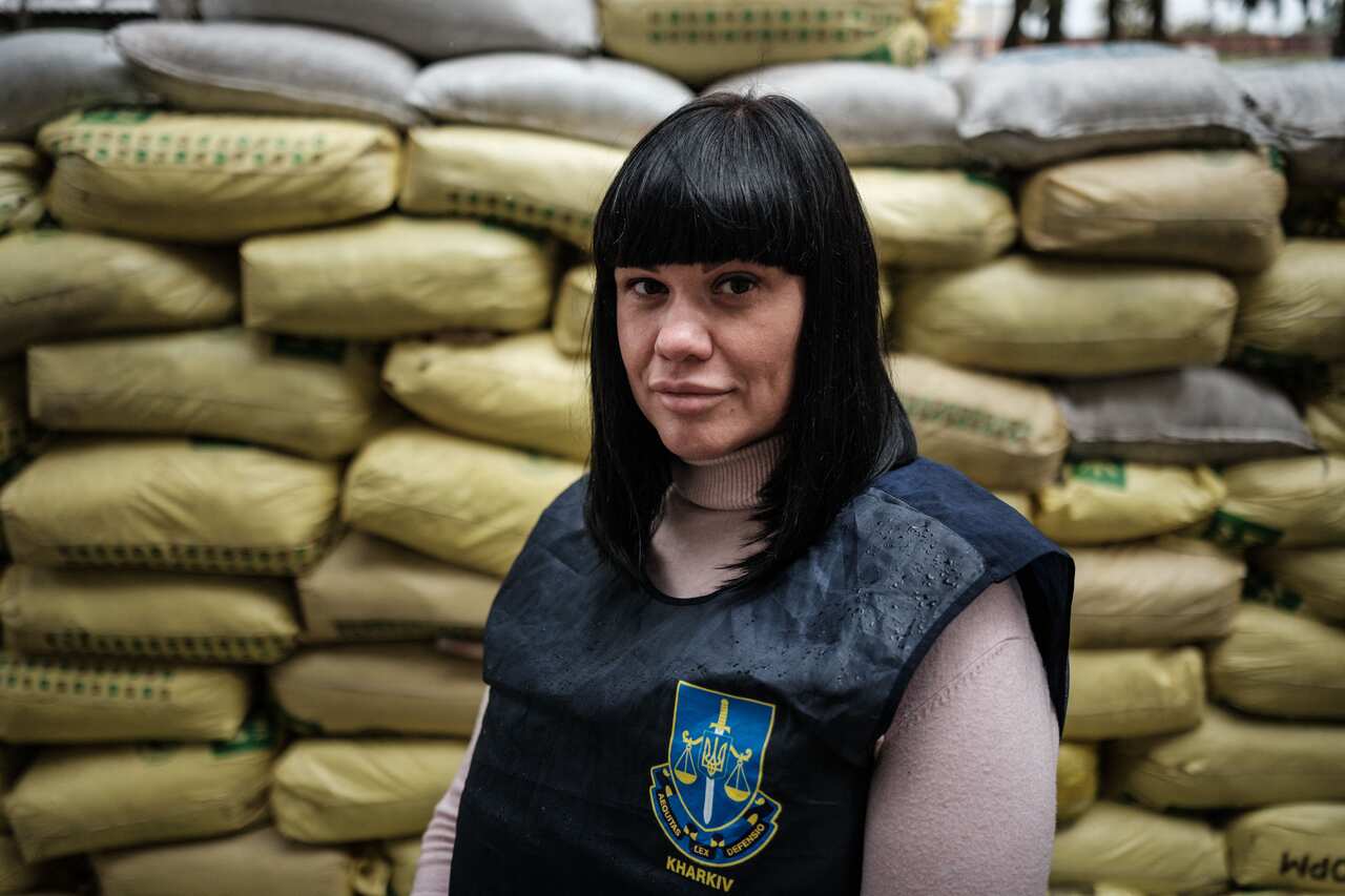 A woman with black hair poses in front of a pile of sandbags