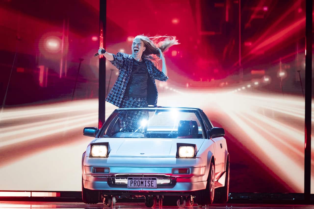 A man with long hair singing on stage in a car 