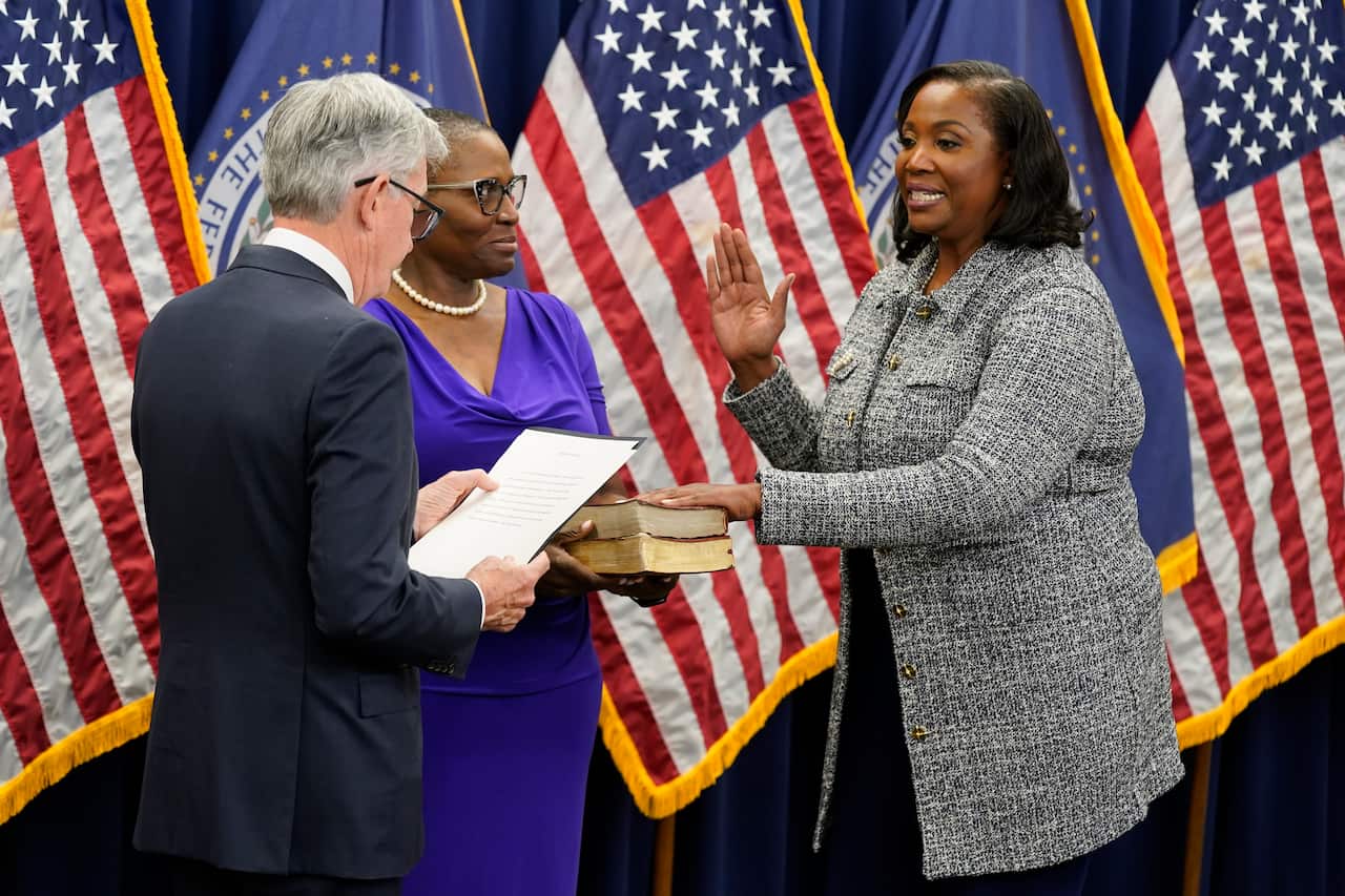 Lisa Cook (right) in a grey jacket is sworn in as Fed Reserve Governor by Jerome Powell (left) in a black jacket in front of American flags and bibles.