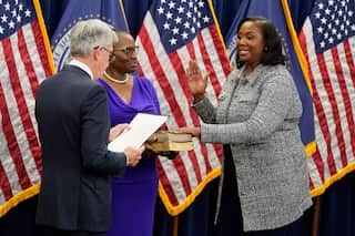 Lisa Cook (right) in a grey jacket is sworn in as Fed Reserve Governor by Jerome Powell (left) in a black jacket in front of American flags and bibles.