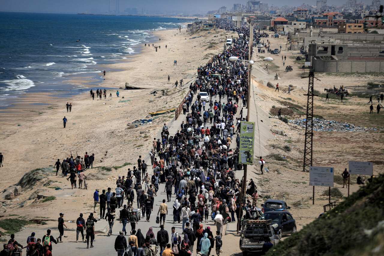 Thousands of Palestinian people walk along a path next to a beach.