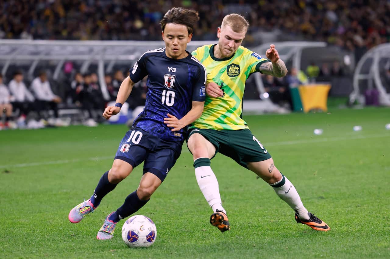 Two footballers, one in a blue strip and the other in a yellow and green strip, compete for the ball