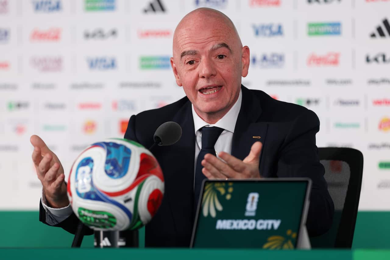 A bald middle-aged white man speaking at a table. A football and electronic tablet is in front of him.