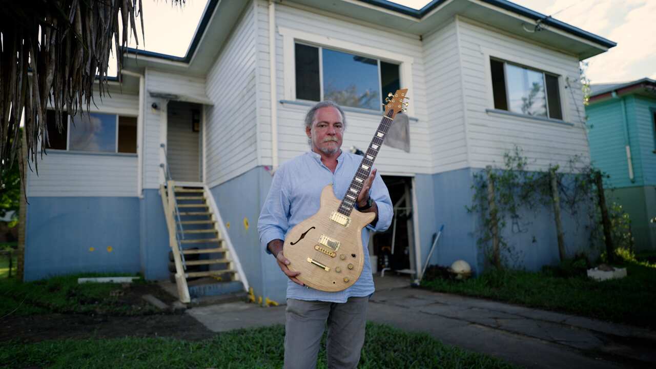Gary Shallala-Hudson stands with one of his guitars outside his inundated home.