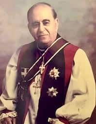 A formal portrait of a man wearing ceremonial clerical vestments, a pectoral cross, and various religious medals.