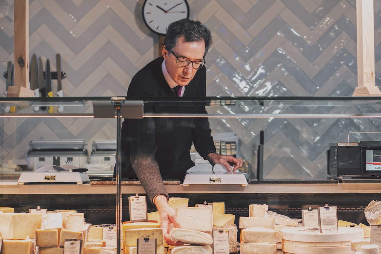 A man stands behind a deli counter full of cheese