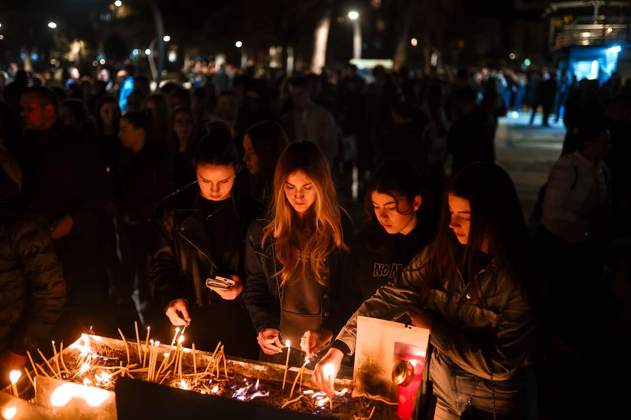Four people light candles at outdoor gathering.