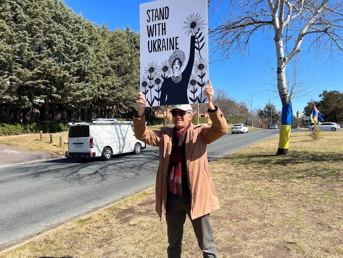 Man holds up sign that says: "Stand with Ukraine". 
