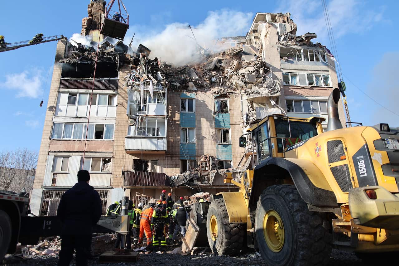 Residential building with large hole in roof and rescue workers out front