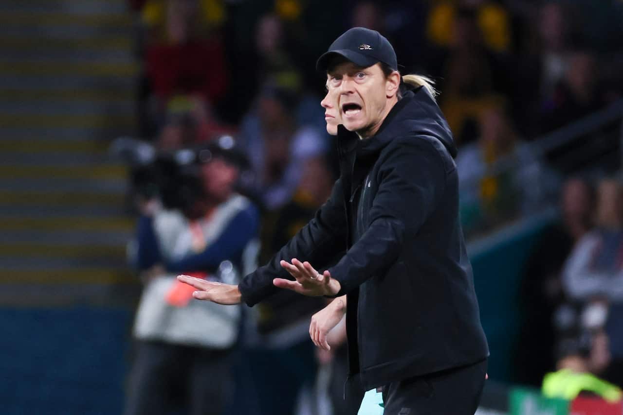 A man in a hat makes a gesture with both his hands stretched out.