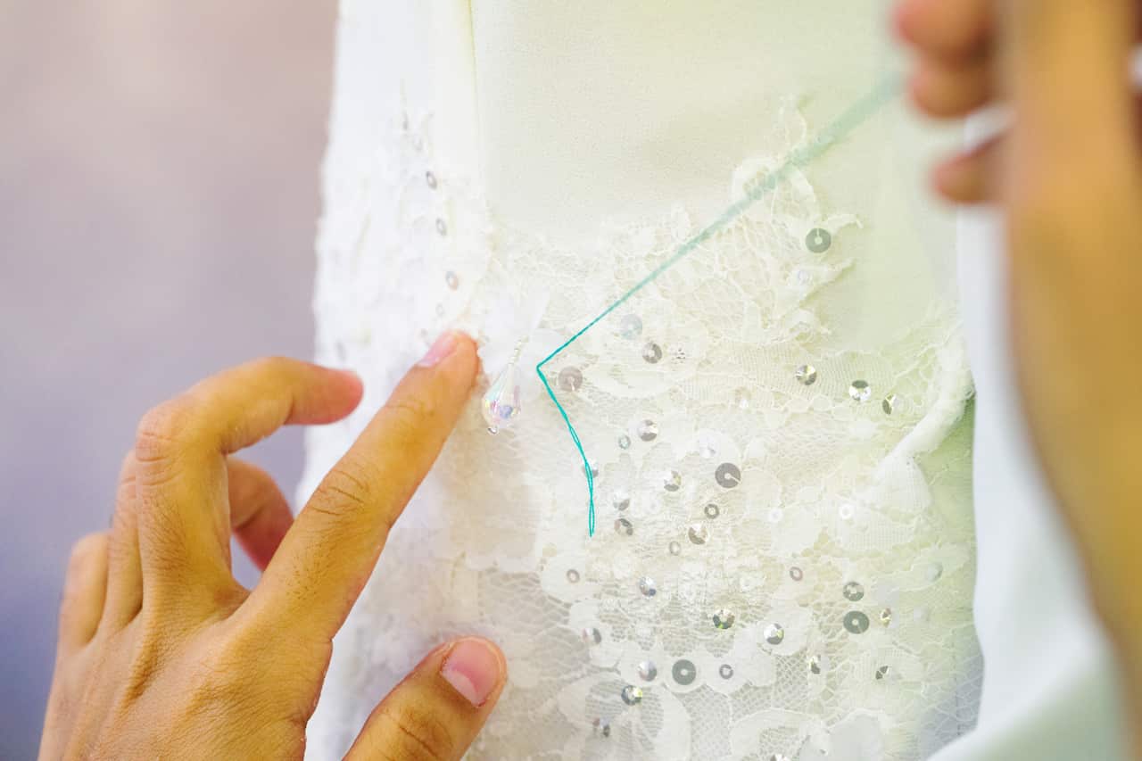 Close-up on female hands sewing wedding dress details