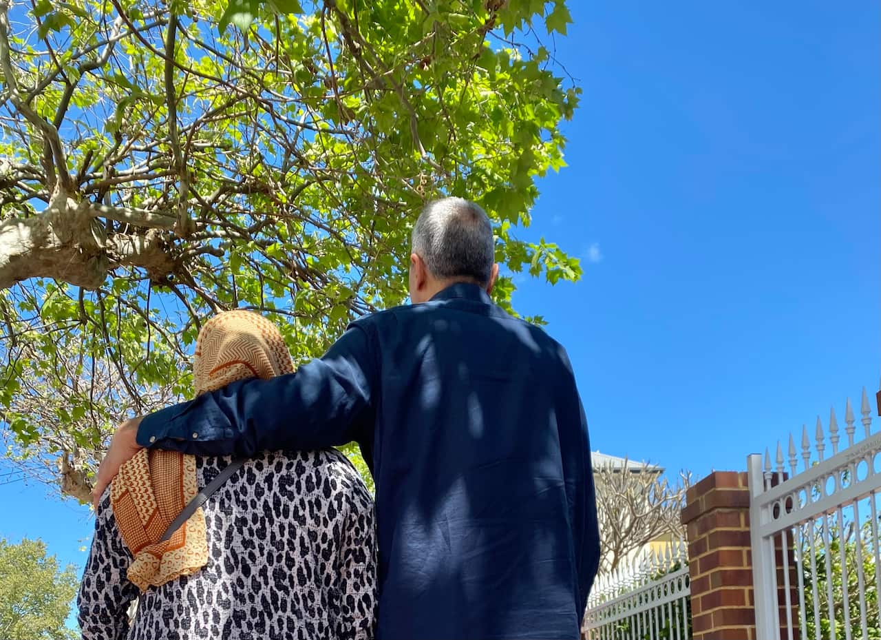 A man with his arm around a woman's shoulder, taken from behind. 