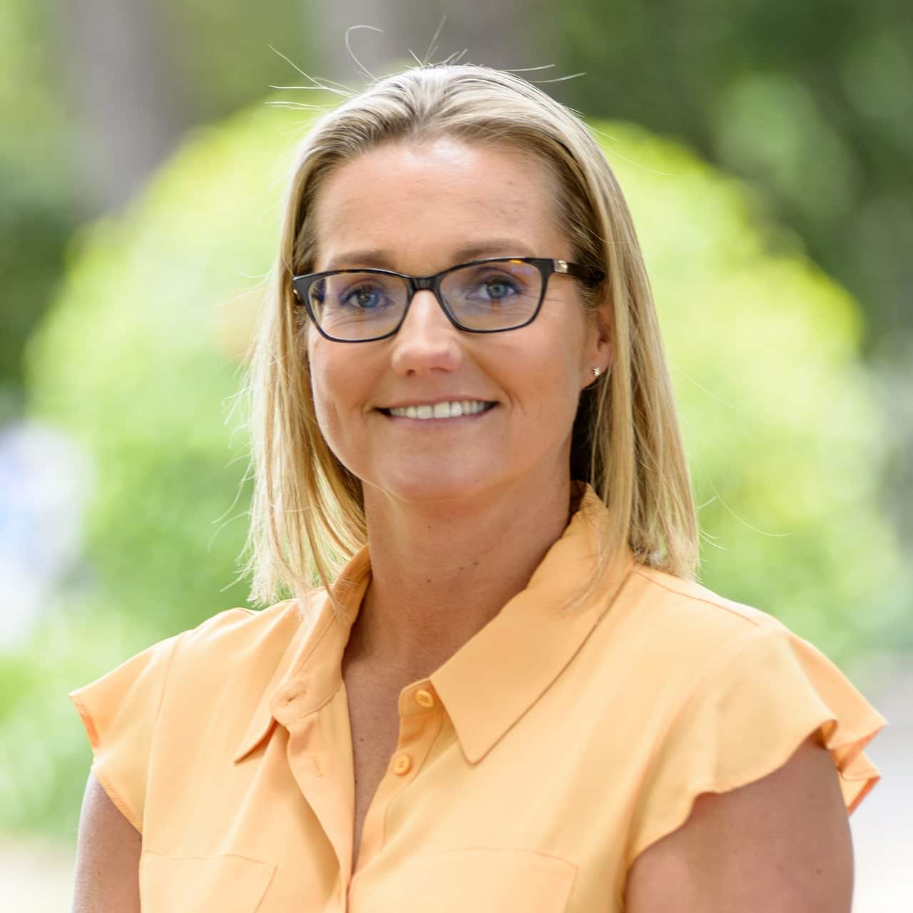 A blonde woman wearing glasses and a yellow blouse