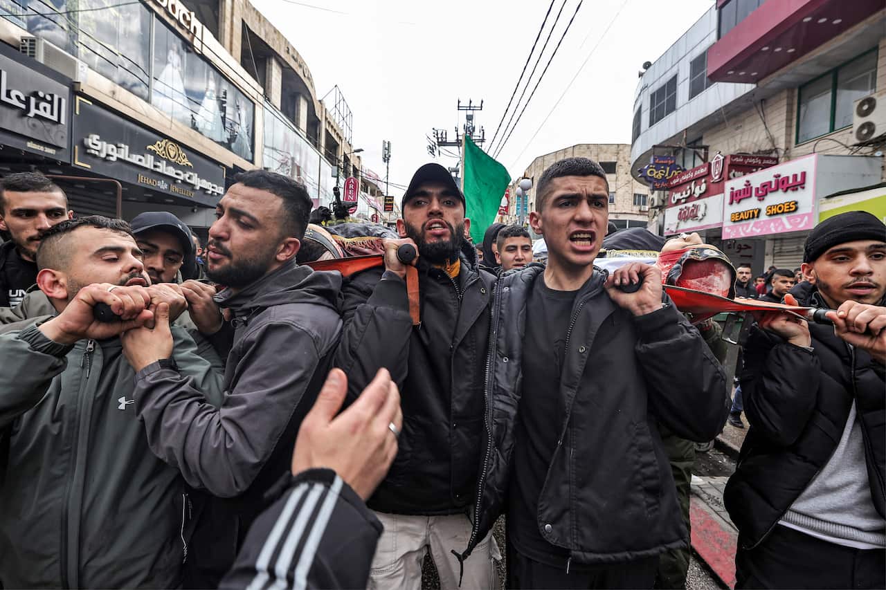People march along a street carrying a stretcher with the bodies of two men who have died.