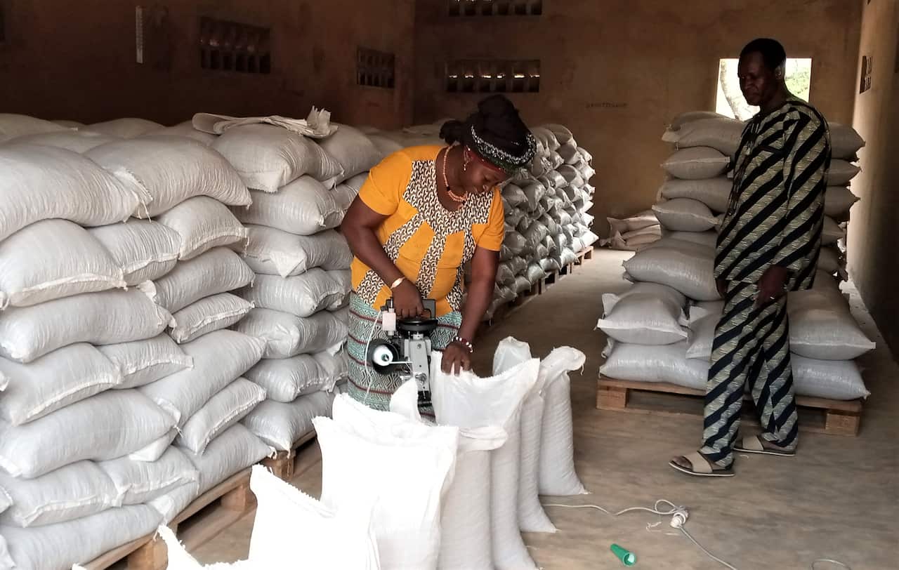 A woman in a warehouse stands over a white bag sealing the top.