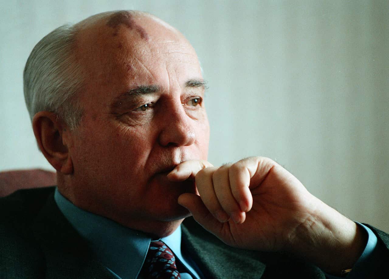 Mikhail Gorbachev looks away, with his hand covering his mouth. 