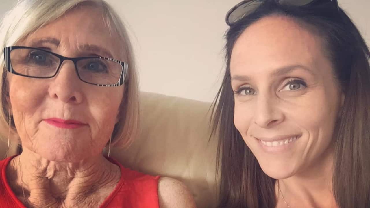a close up of an older woman with grey hair in glasses and a red top on a couch with a young woman with long brown hair