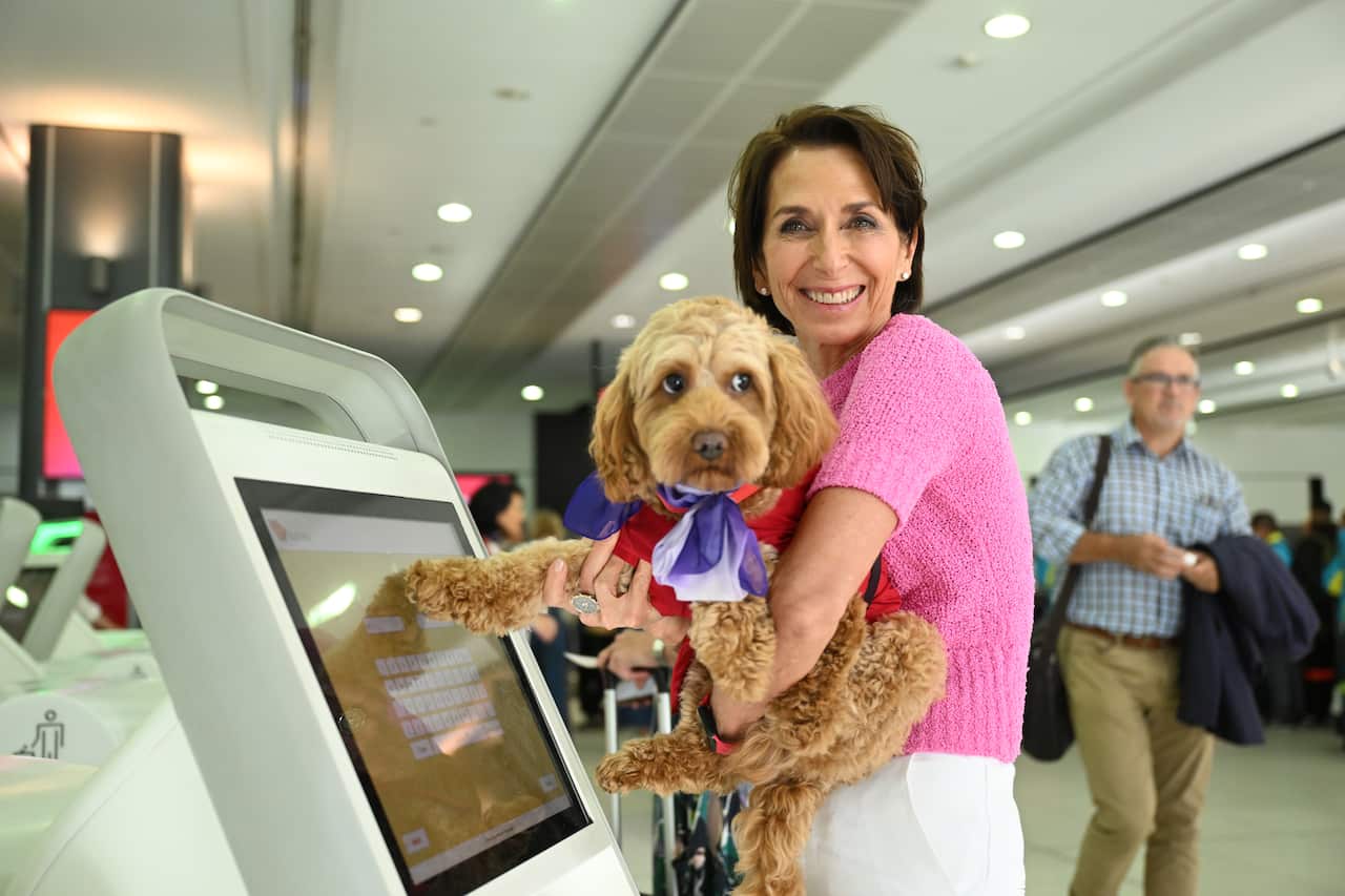 A woman holding a dog and holding its paw gently against a touchscreen device.