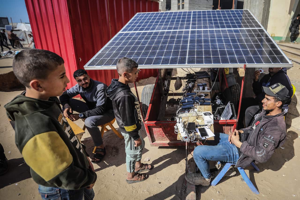 Palestinians charge their phones at a charging station fed by a solar panel in a refugee camp.