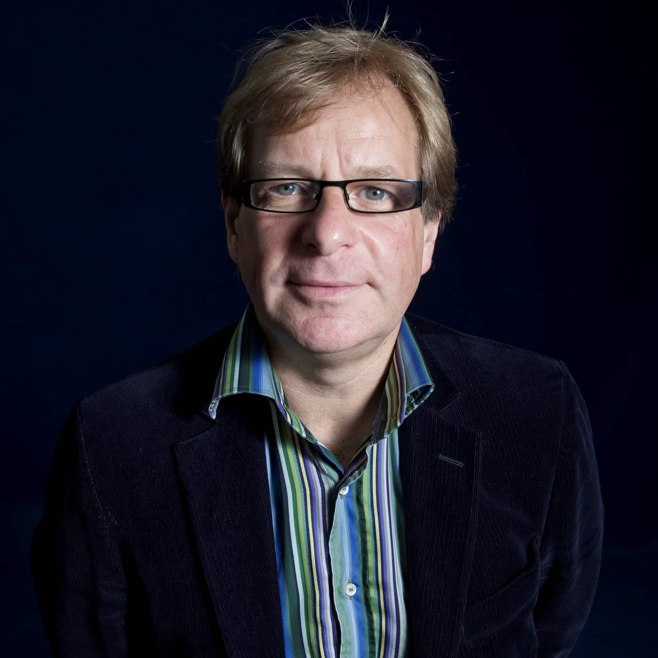 A man wearing glasses with a black frame, a blue and green striped shirt, and a navy cord jacket