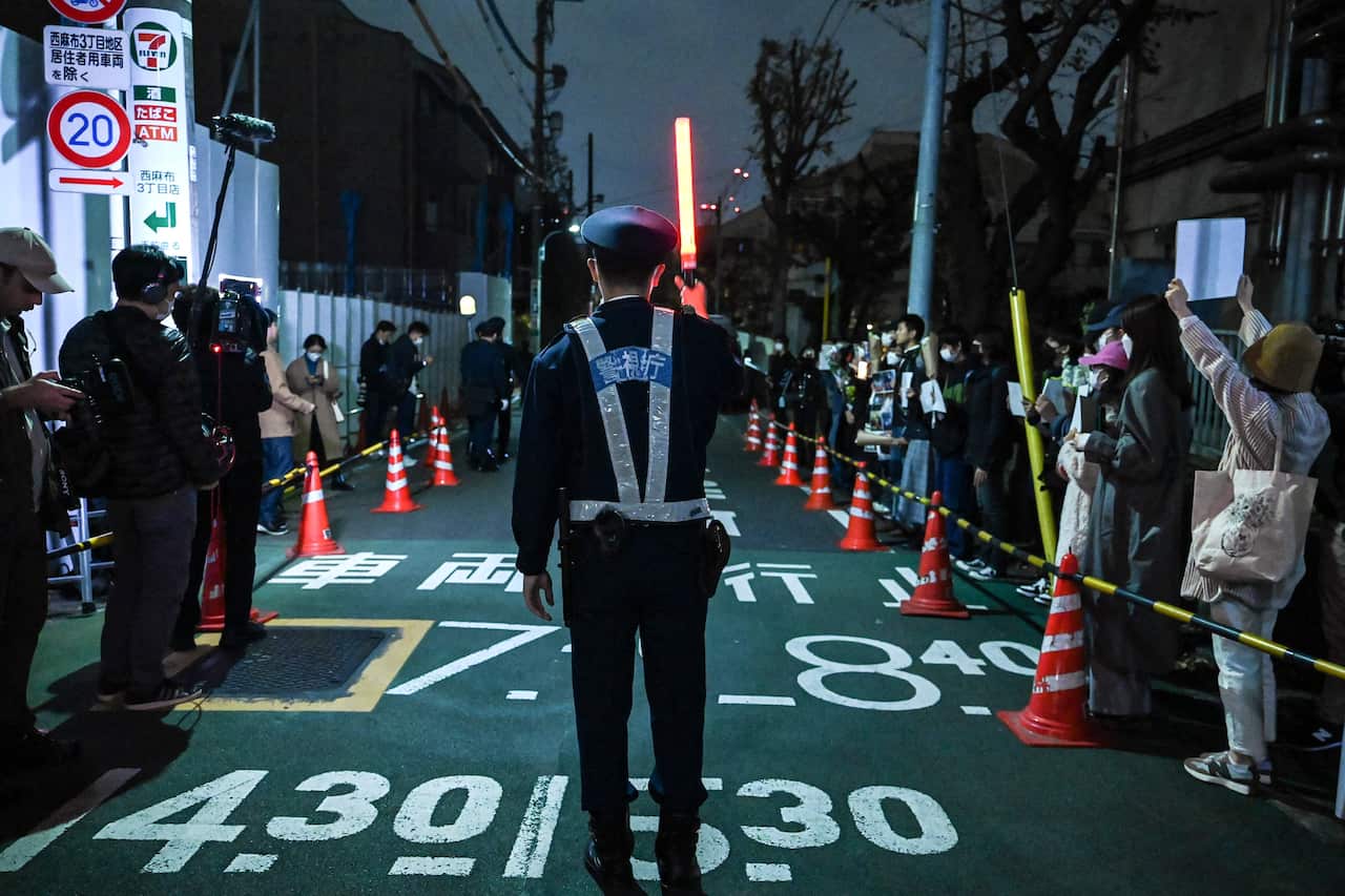 A policeman standing on a road where there is a group of protesters.