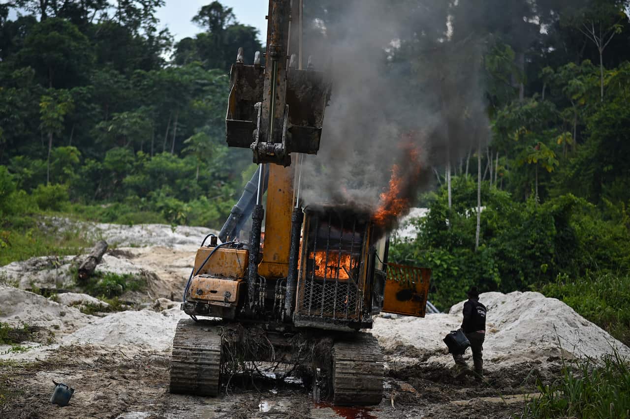 A person standing next to an excavator that is on fire.